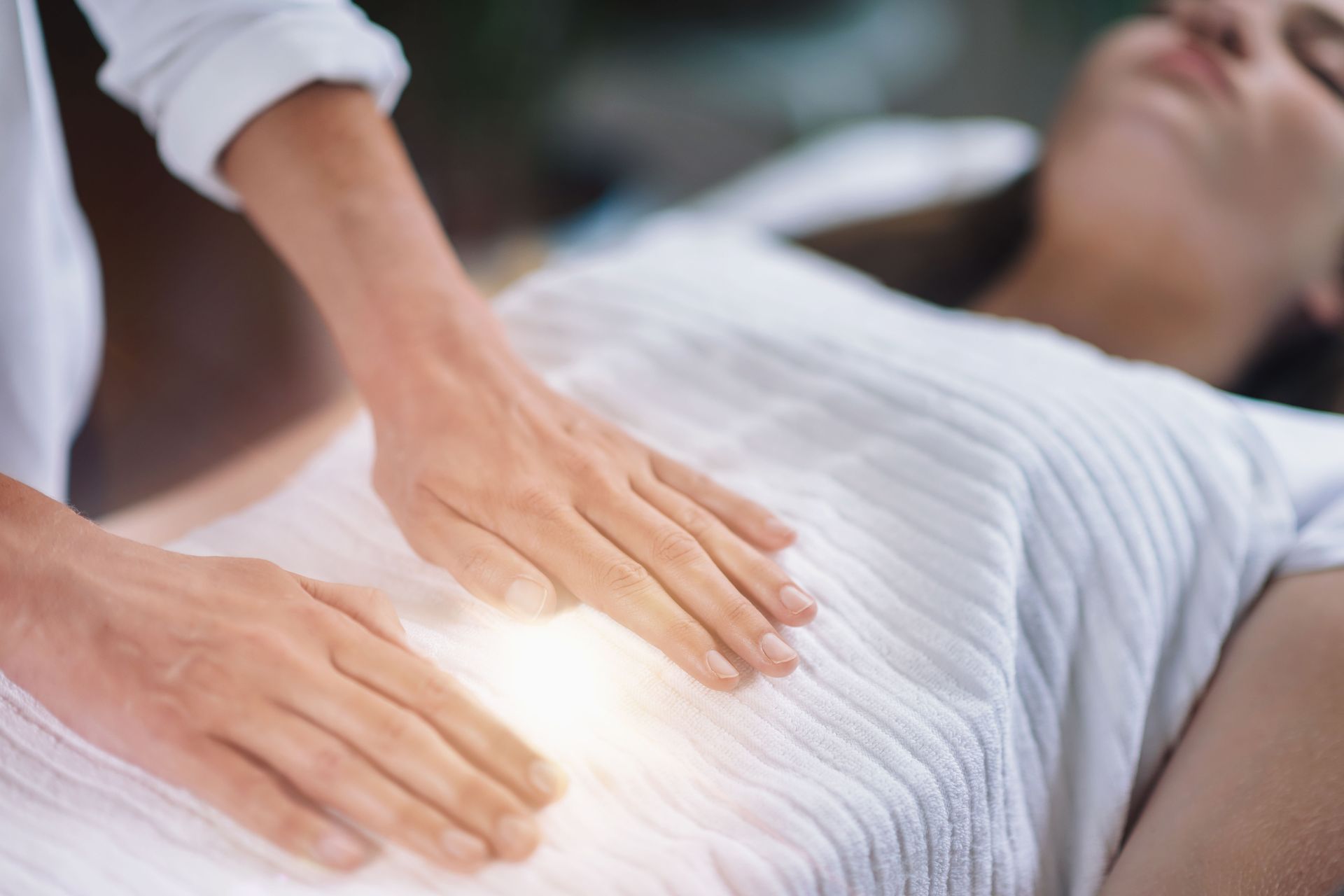 A woman is laying on a bed getting a healing session.