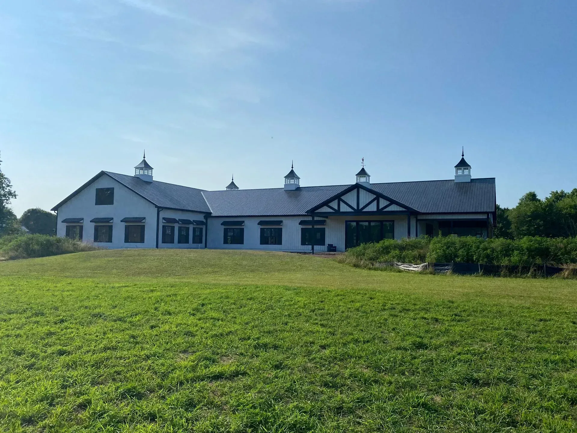 White building with black roof and trim on a green grassy hill under a blue sky.