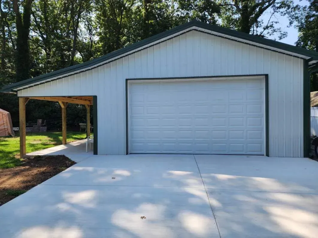 White garage with attached carport, green trim, and concrete driveway.