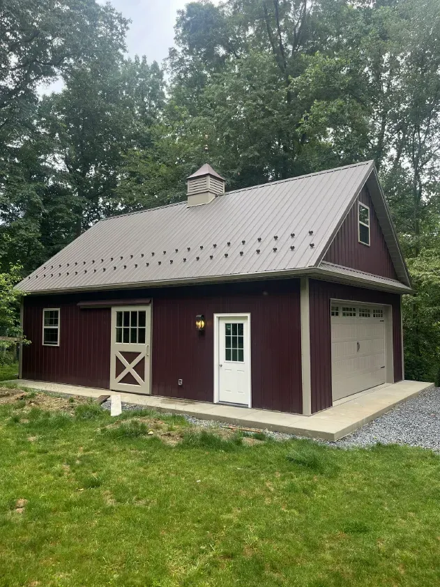 Red barn-style building with tan accents and a metal roof; features a sliding door, garage door, and a small cupola.
