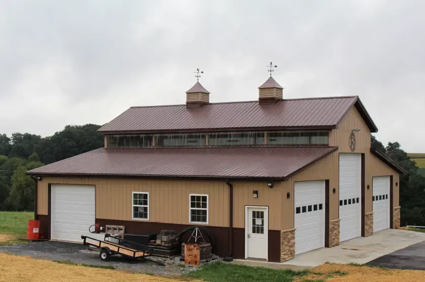 Tan and brown barn with three garage doors and a loft, set against a cloudy sky.