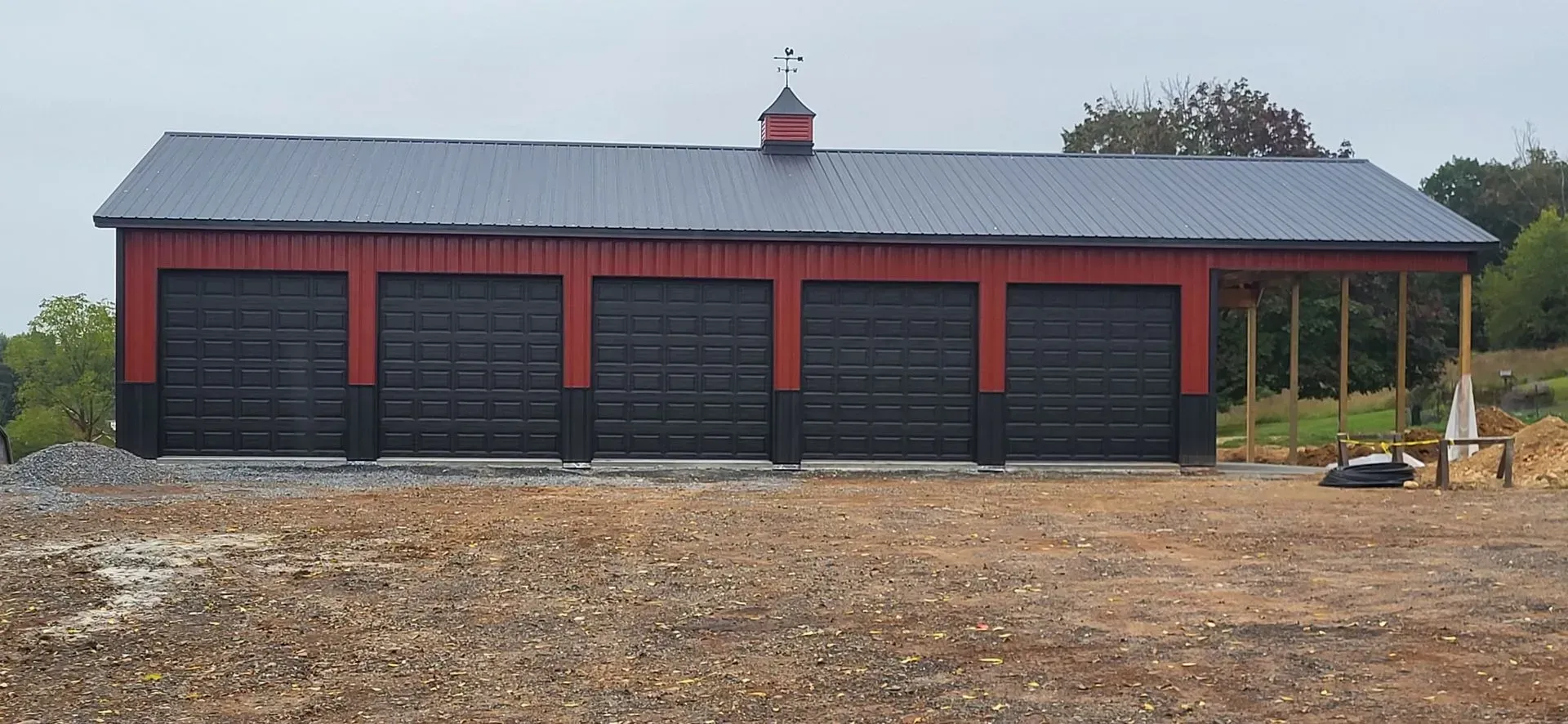 Red and black garage building with black roof and weathervane.