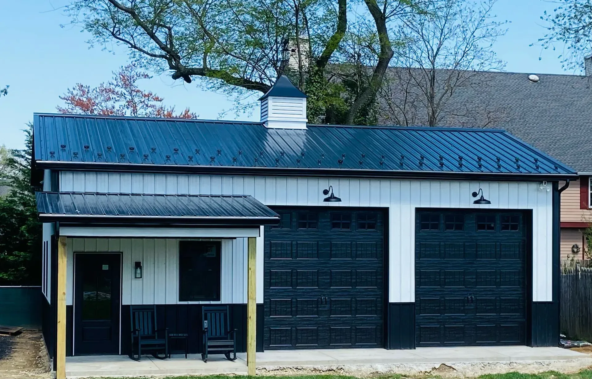 Two-car garage with a matching side room, featuring a black metal roof, white siding, and black garage doors.