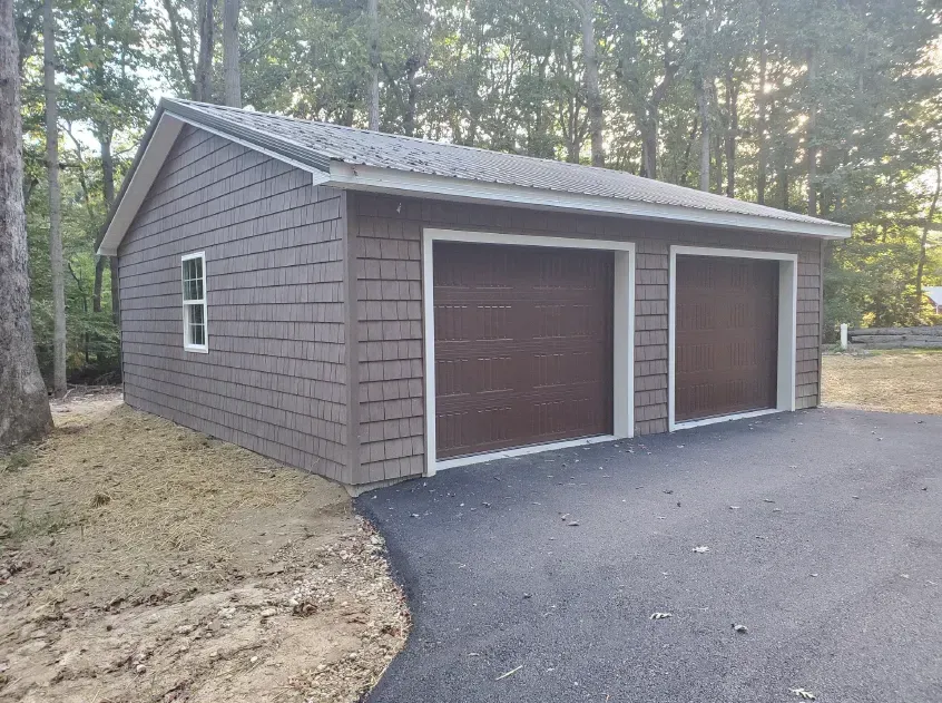 Brown-sided two-car garage with brown doors, white trim, and a gray roof, set on an asphalt driveway.