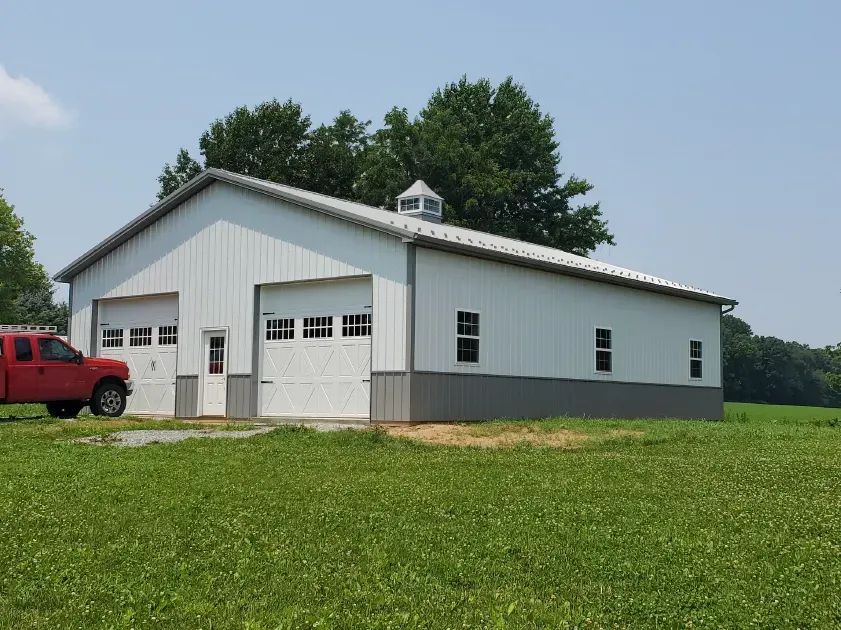 White metal building with gray accents, red truck parked beside it, on a grassy field.