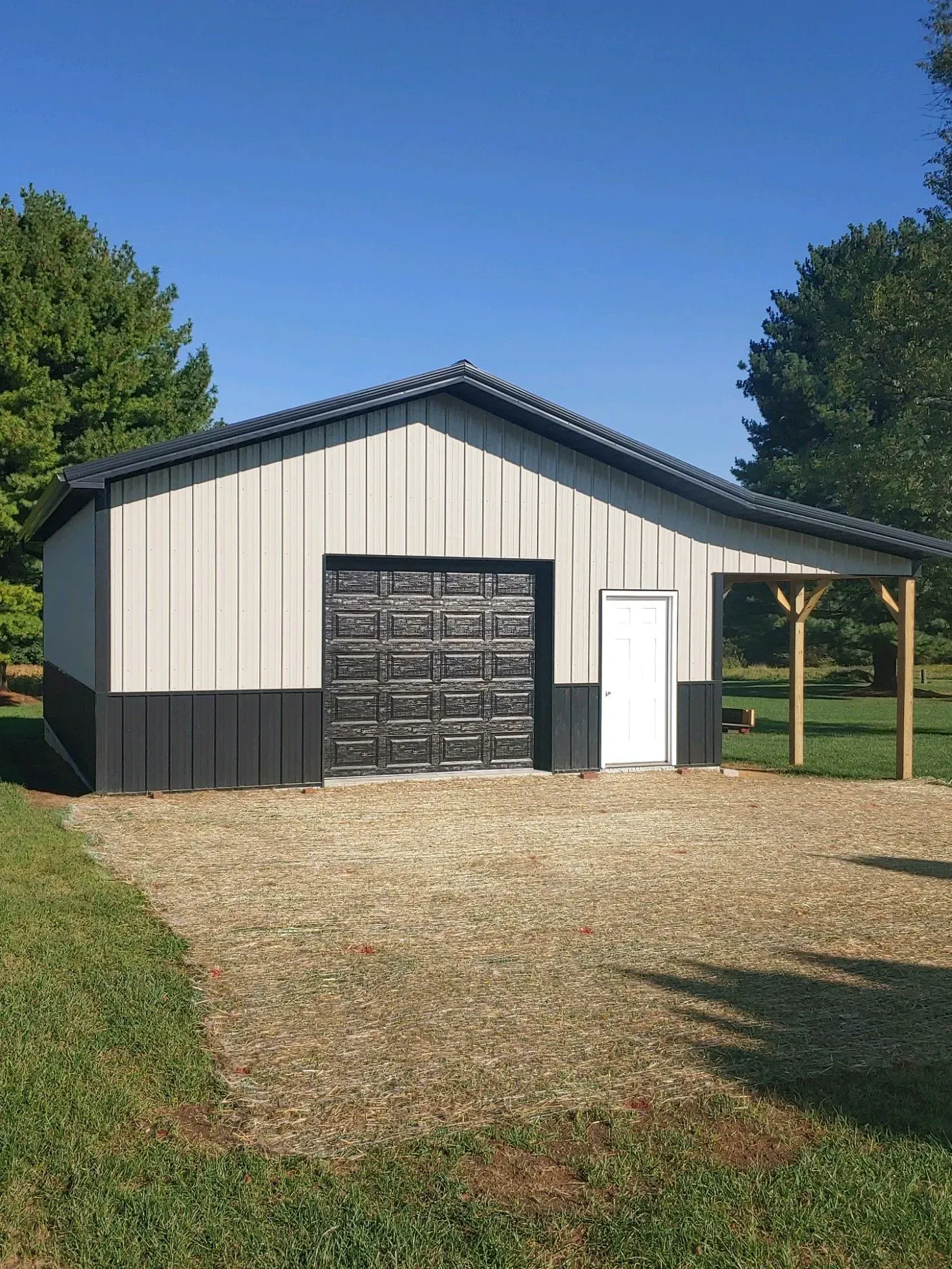 Metal barn with gray and black siding, gravel driveway, and a small porch.