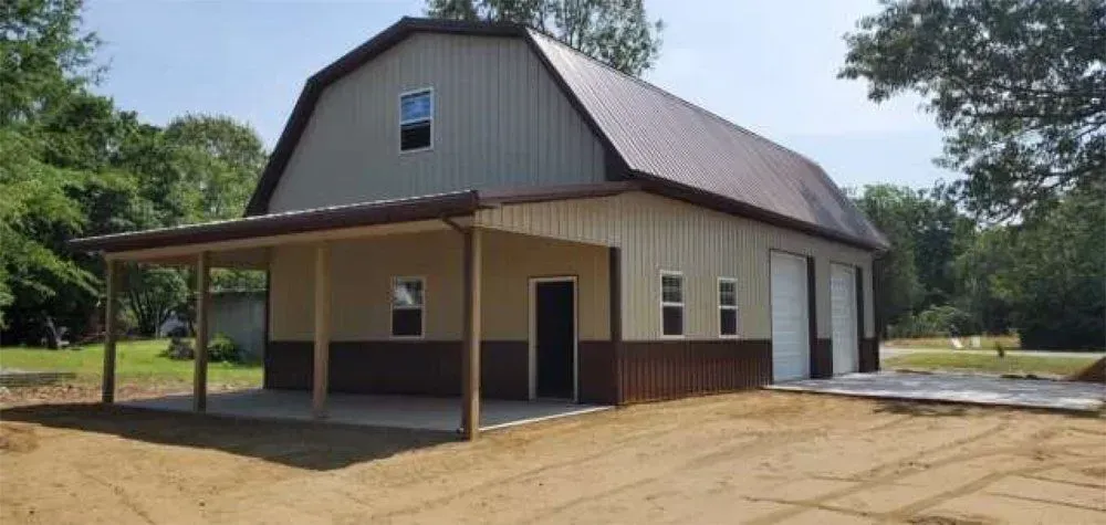 A two-story barn with a covered porch. Tan and brown exterior, metal roof, and two garage doors.