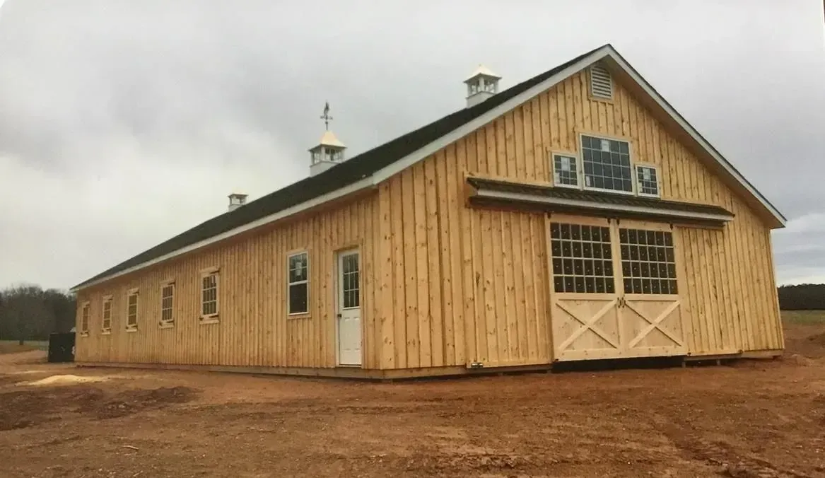 New wooden barn with white doors and windows, under a cloudy sky.