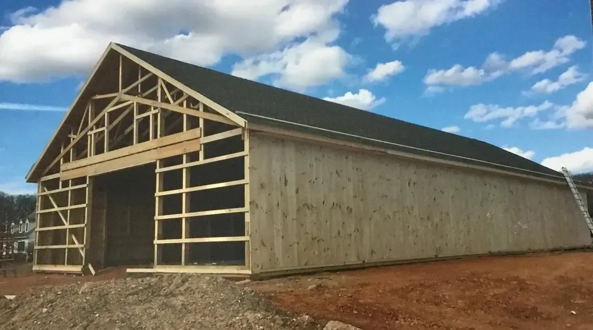 Wooden barn under construction with dark roof, open doorway, blue sky background.