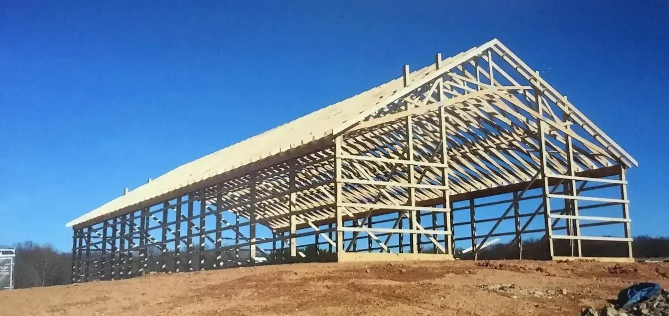 Wooden barn frame under construction against a clear blue sky.