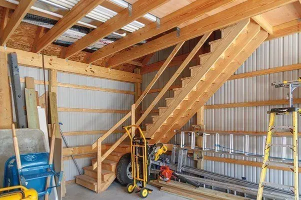 Wooden stairs in a garage-like structure with corrugated metal walls; handrail and tools visible.