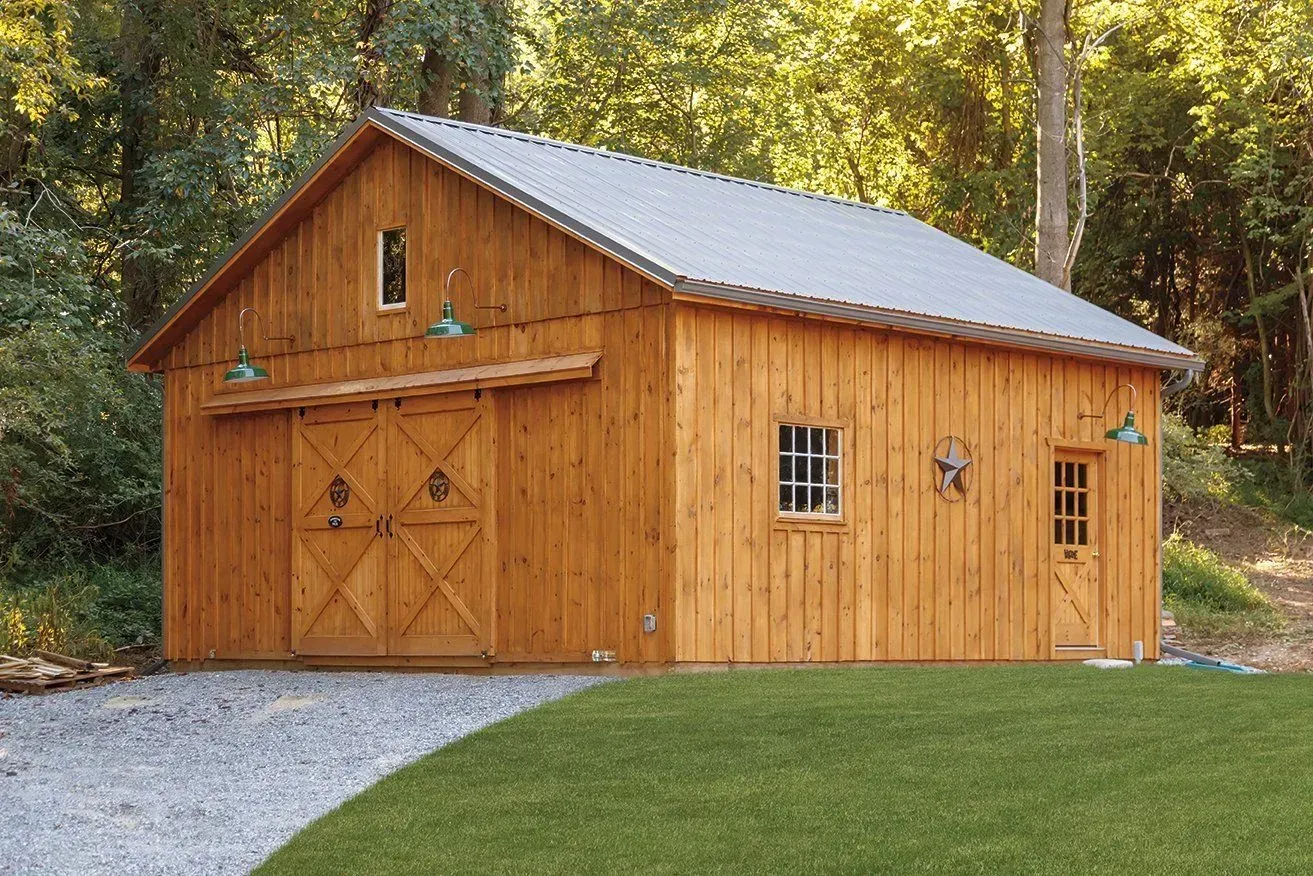Wooden barn with a metal roof, two large doors, and a side door, set on gravel.