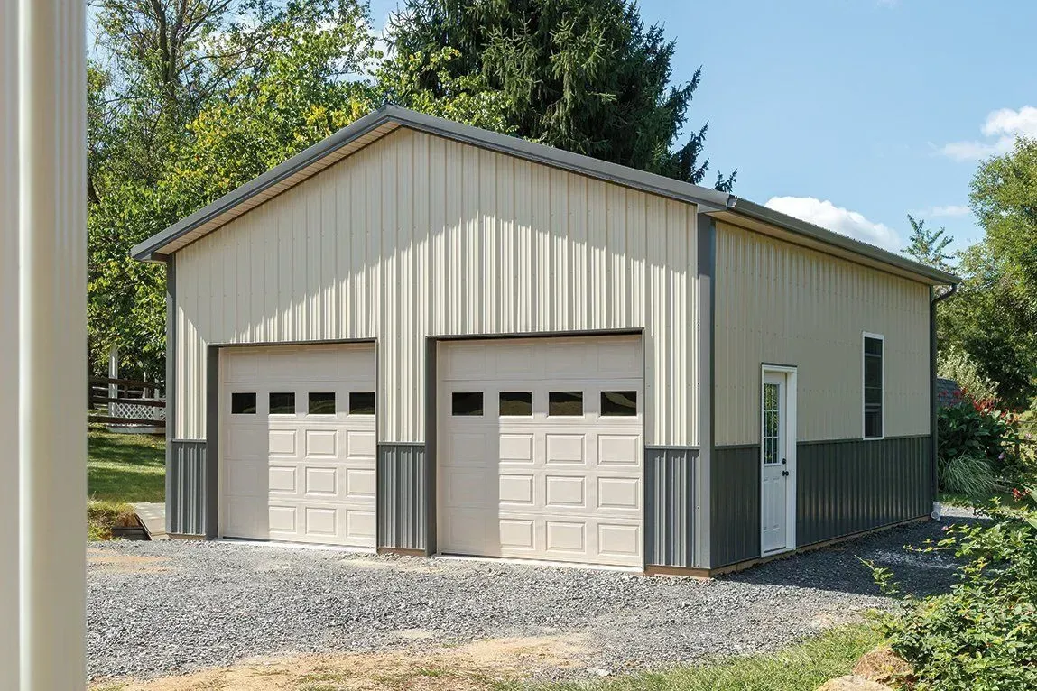 Two-car garage with beige siding, gray trim, and two garage doors. Gravel driveway, blue sky.