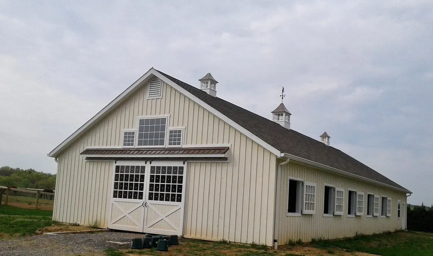 White barn with dark roof and multiple windows under a cloudy sky.