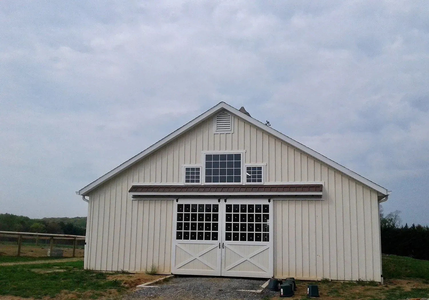 White barn with sliding doors and small windows under a cloudy sky.
