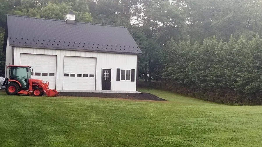 White two-bay garage with black roof; orange tractor on the left.