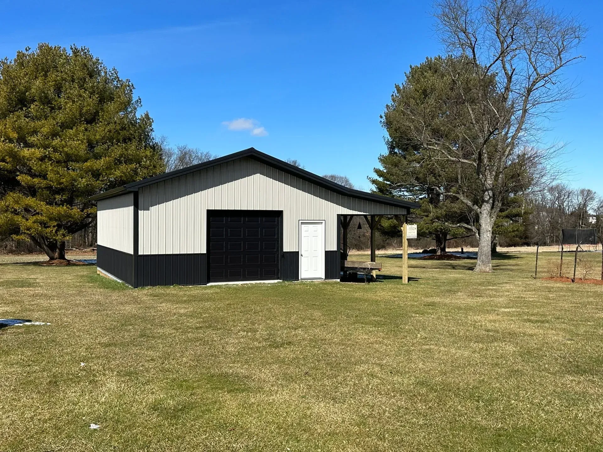 Barn with black and gray siding, black roof, and white door under a blue sky.