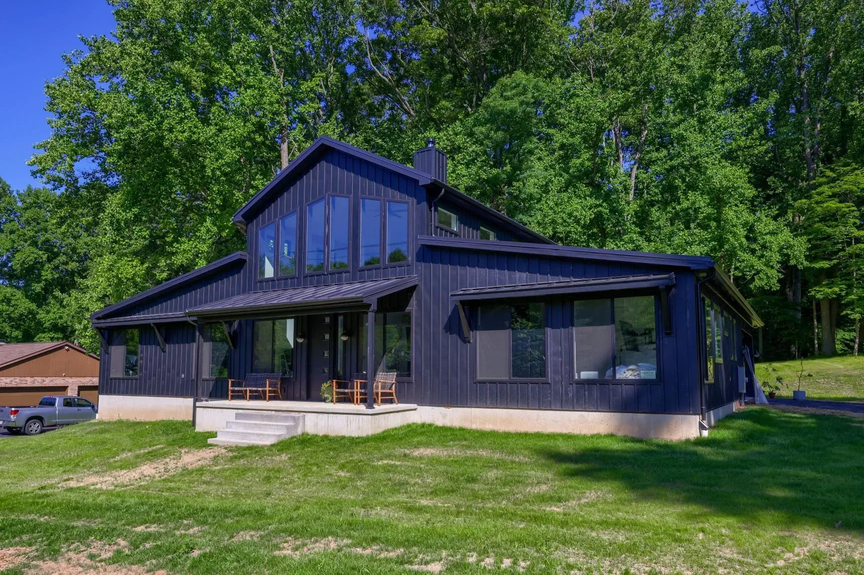 Black modern house with large windows, set in a green grassy yard with trees in the background.