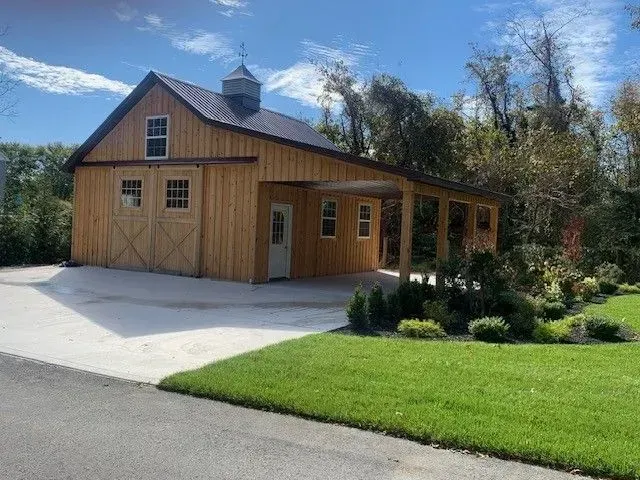 Tan barn with a covered porch, two doors, and a concrete driveway. Sunny day.
