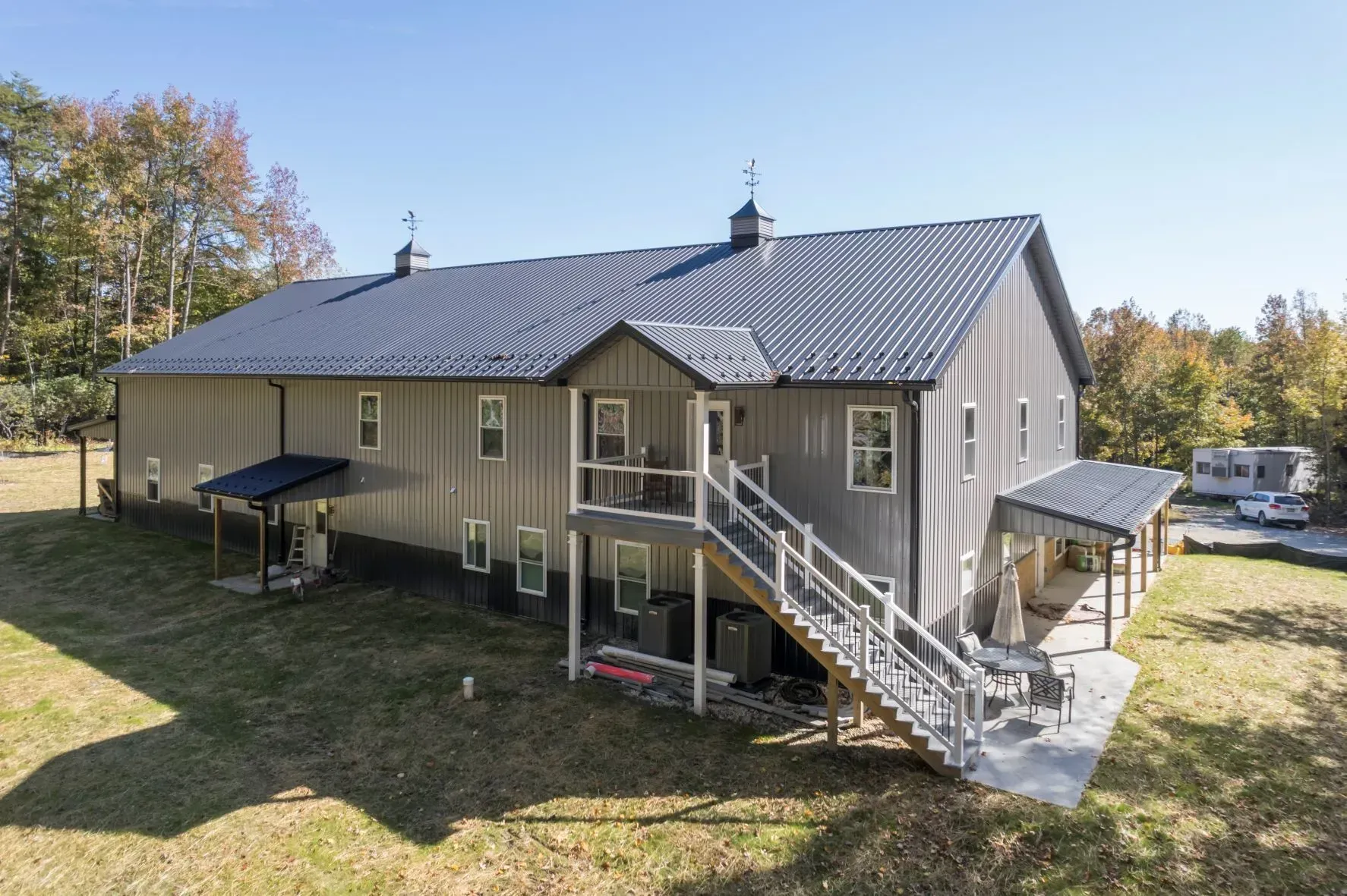 Gray barn-style house with dark roof and multiple entrances, set on grassy land under a blue sky.