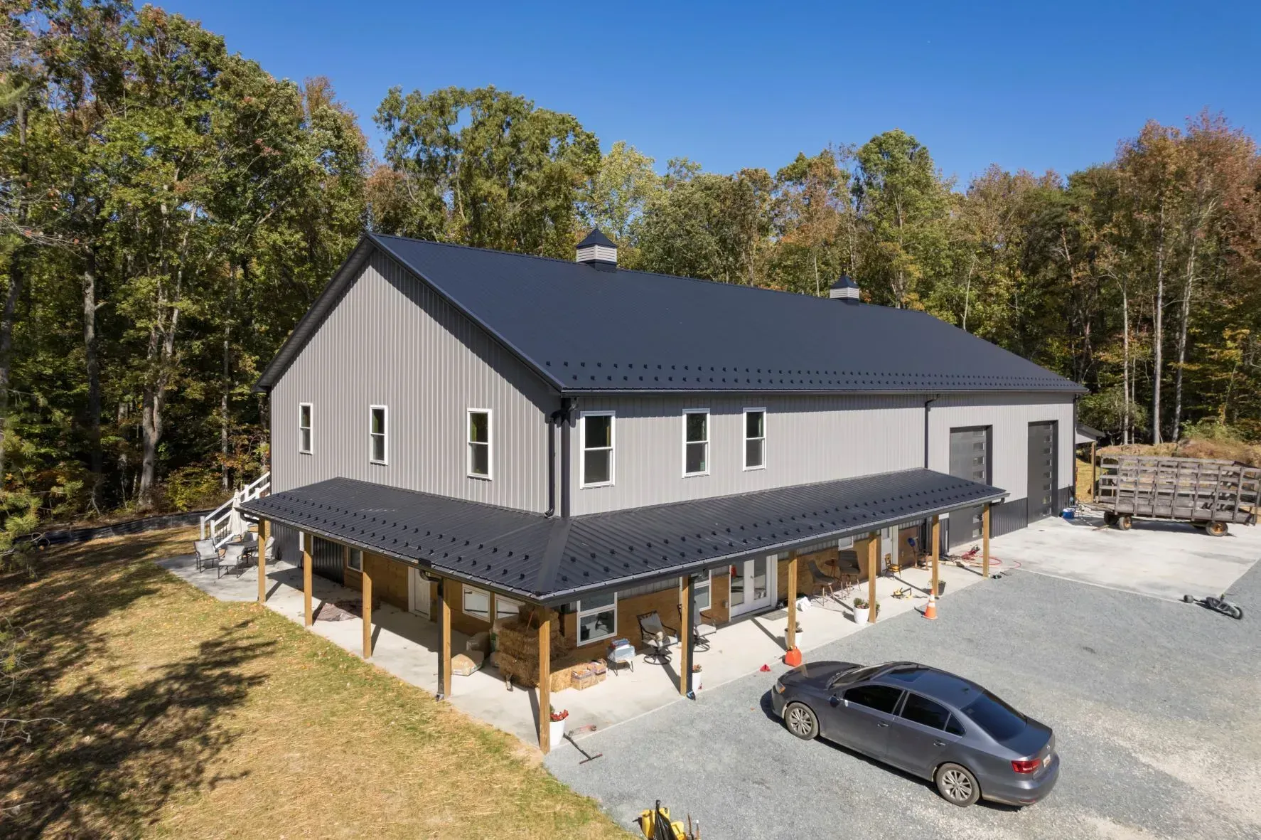 Gray barn-style building with a dark roof and a porch. A car is parked on gravel in front.