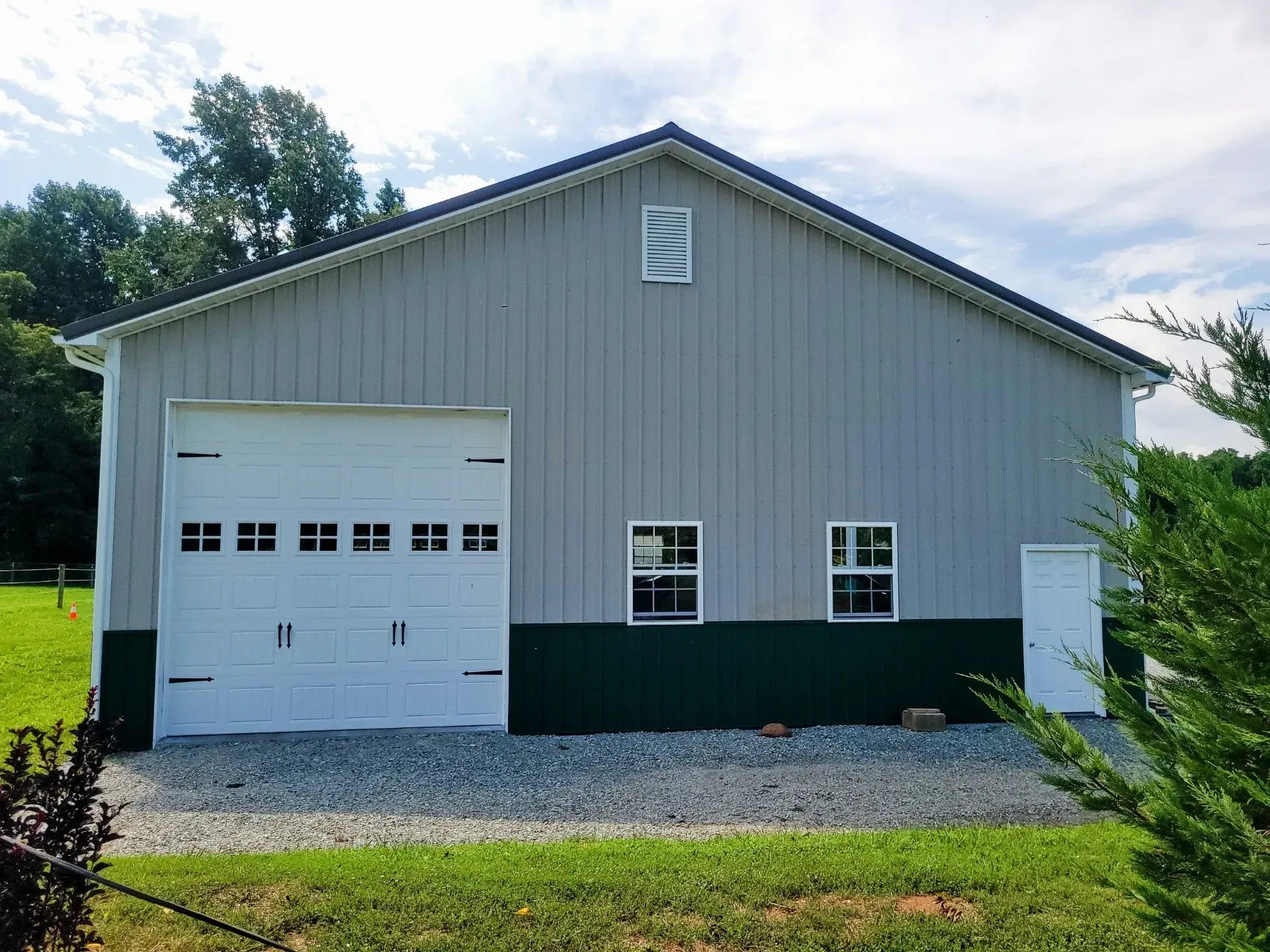 Gray and green metal building with a white garage door, two windows, and a small white door.