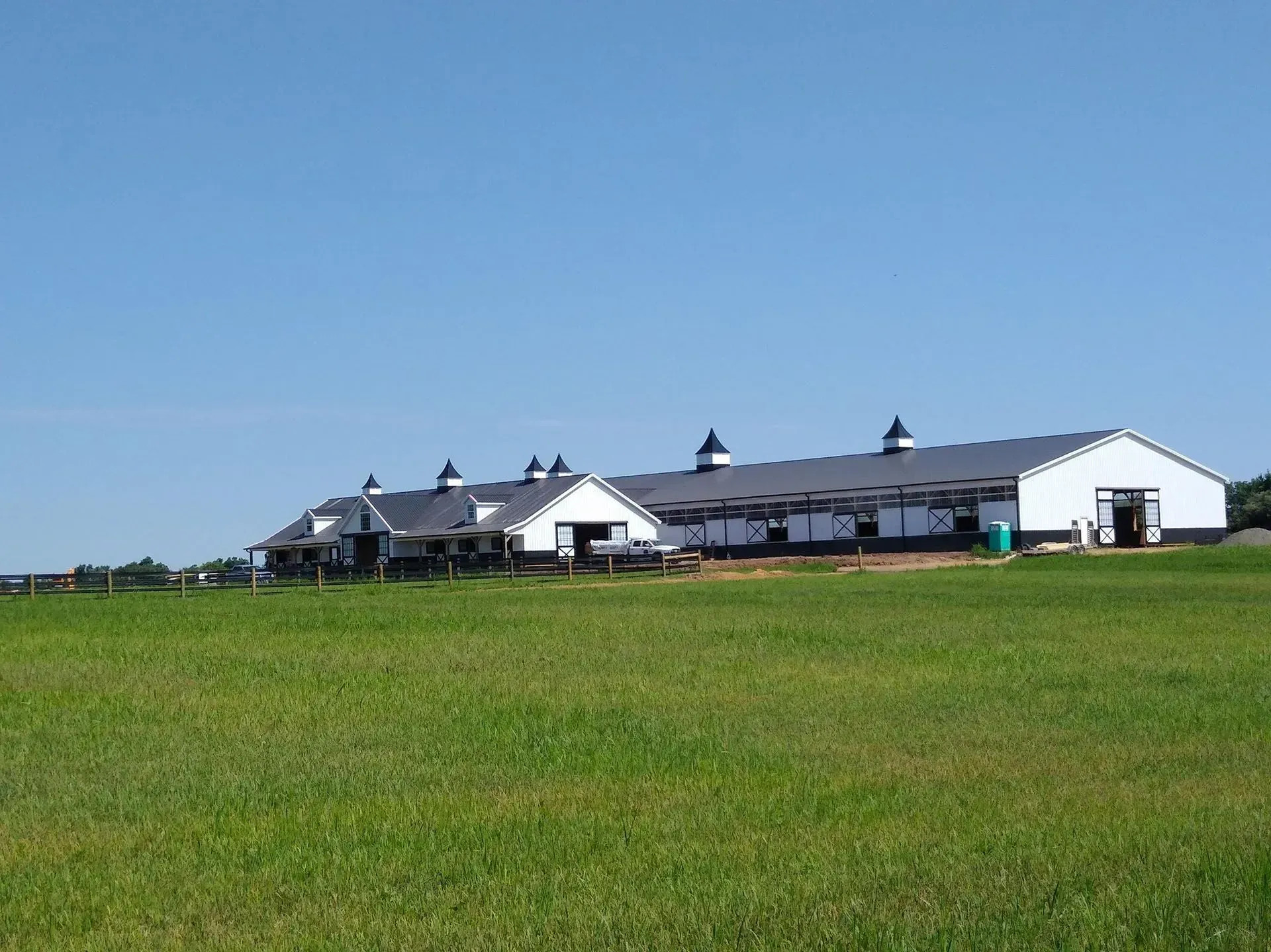 White barn with black accents, set against a bright blue sky and green field.