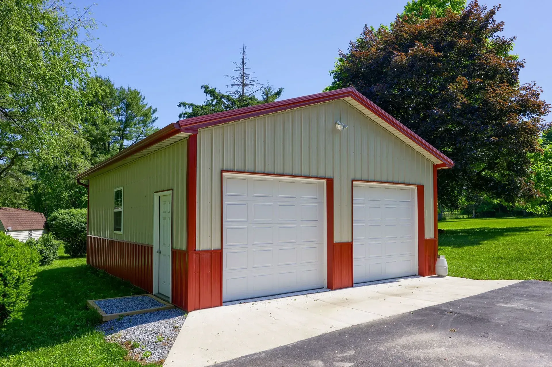 Two-car garage with red trim, white doors, and a concrete driveway on a sunny day.