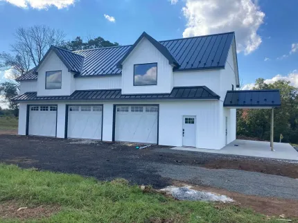 White modern farmhouse with black roof and garage doors on a gravel driveway.