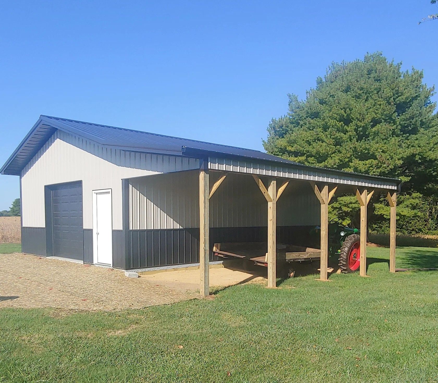 Gray and black metal barn with covered wooden porch. A tractor is parked under the porch.