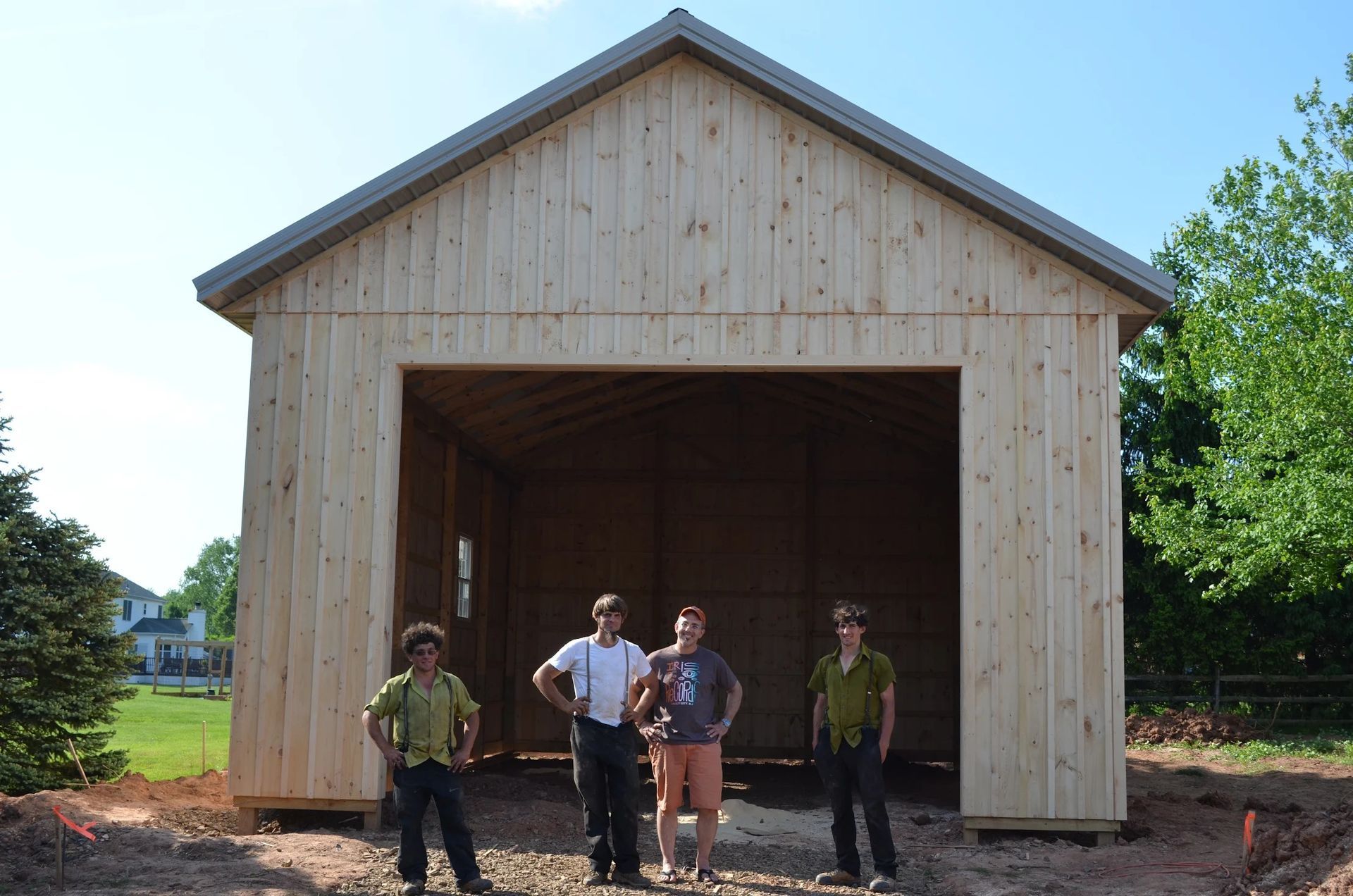 Four people standing in front of a newly built wooden structure with a large opening, sunny day.
