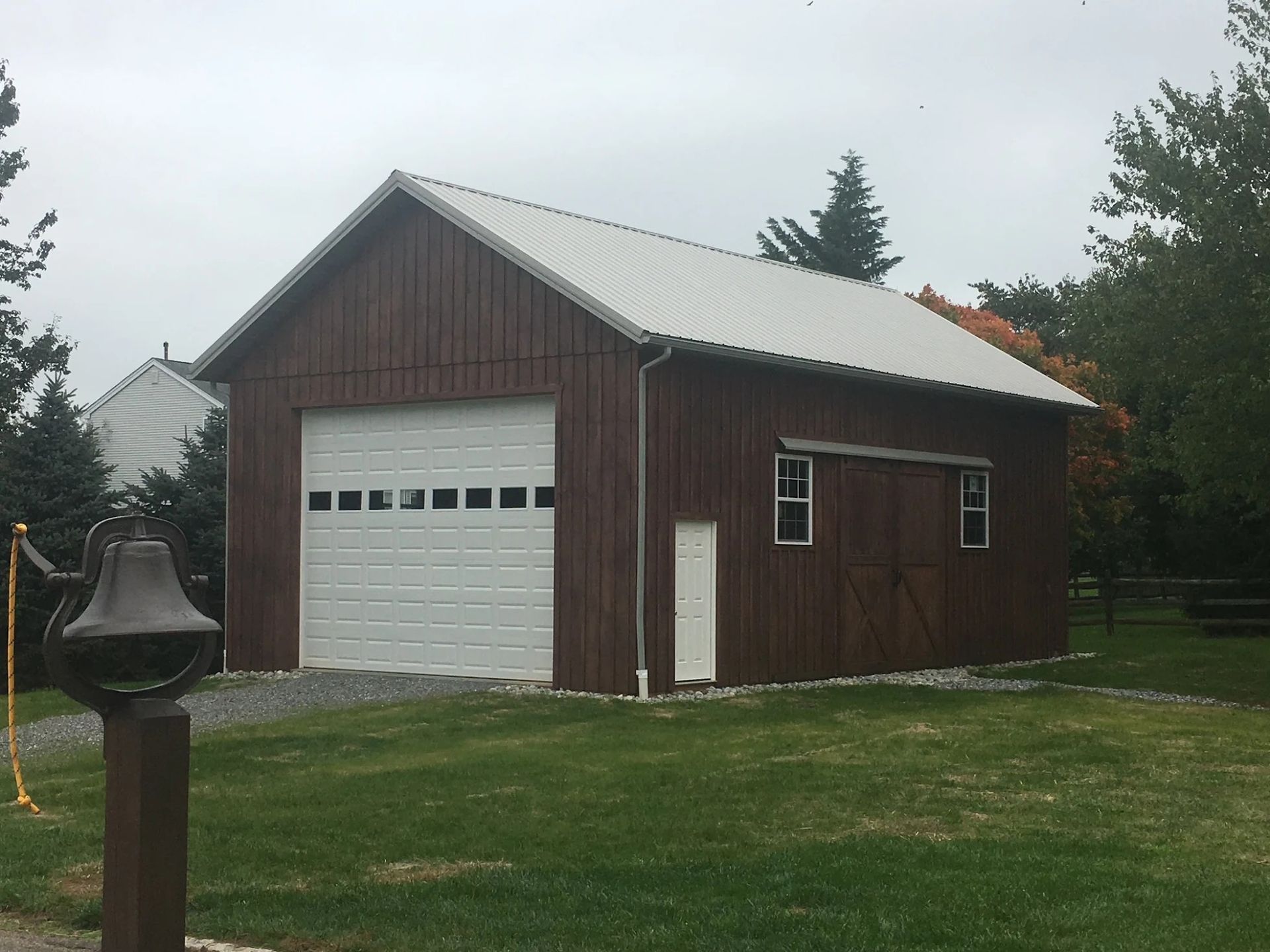 Brown barn with white garage door and metal roof on a grassy lawn.