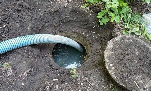 Blue hose draining muddy water into a hole in the ground beside a concrete cover.