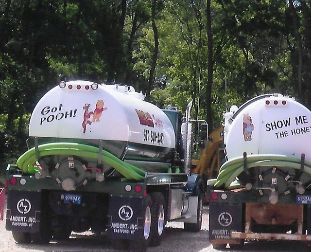 Two decorated white tanker trucks in a wooded area, one reading “GO! POOH!” and the other “SHOW ME THE HONEY!”