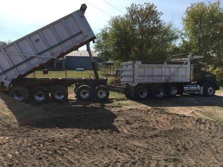 Two dump trailers parked on a dirt lot, one raised to unload gravel or soil.