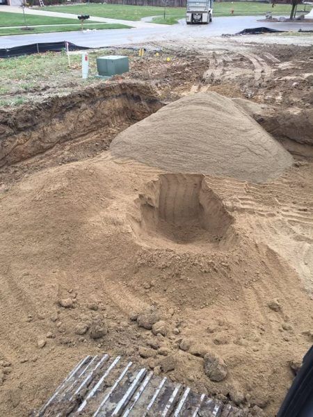 Excavation site with dirt mounds, a deep hole, and construction materials near a roadway.