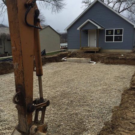 Gravel yard under construction with a blue house in the background and a utility pole in the foreground