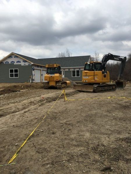 Construction site with two yellow excavators in front of a gray house under construction.