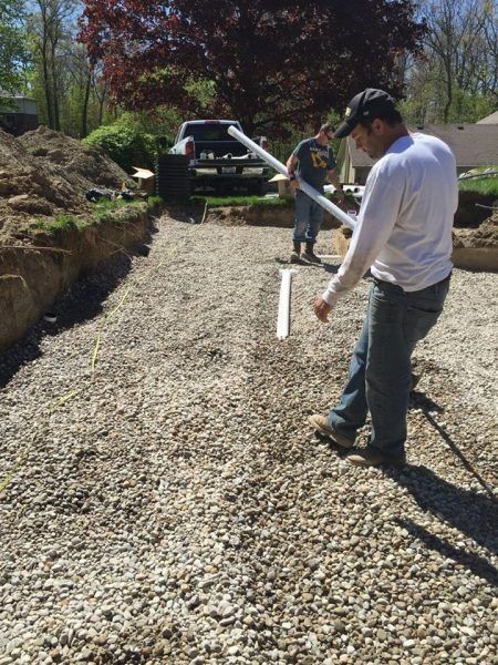 Workers measuring a gravel driveway beside an SUV on a sunny construction site
