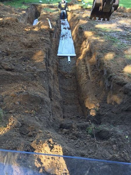 Excavator placing a metal trench cover over a deep dug trench in a wooded area