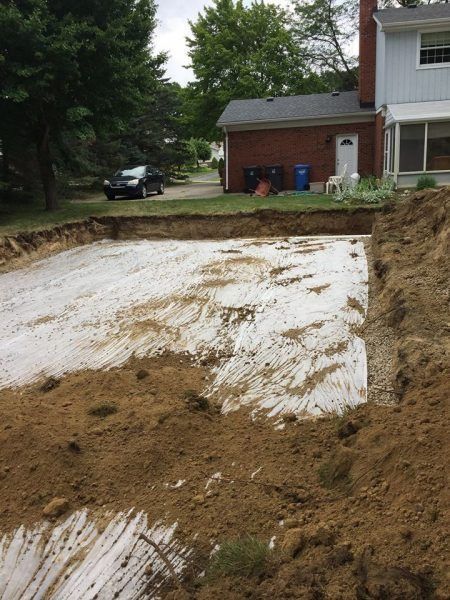 Excavated backyard foundation pit beside a brick house, with dirt walls and white ground cover.
