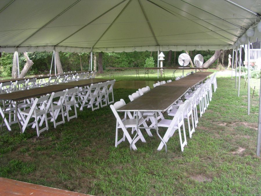 A long table with white chairs under a tent