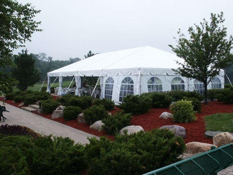 A large white tent is surrounded by bushes and rocks