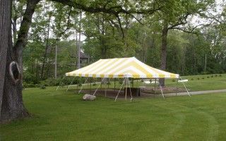 A yellow and white tent is sitting in the middle of a grassy field.