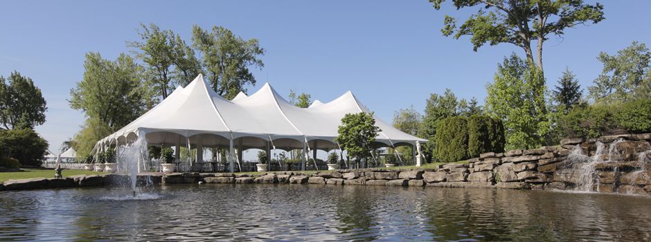 A large white tent is sitting next to a pond with a waterfall in the background.