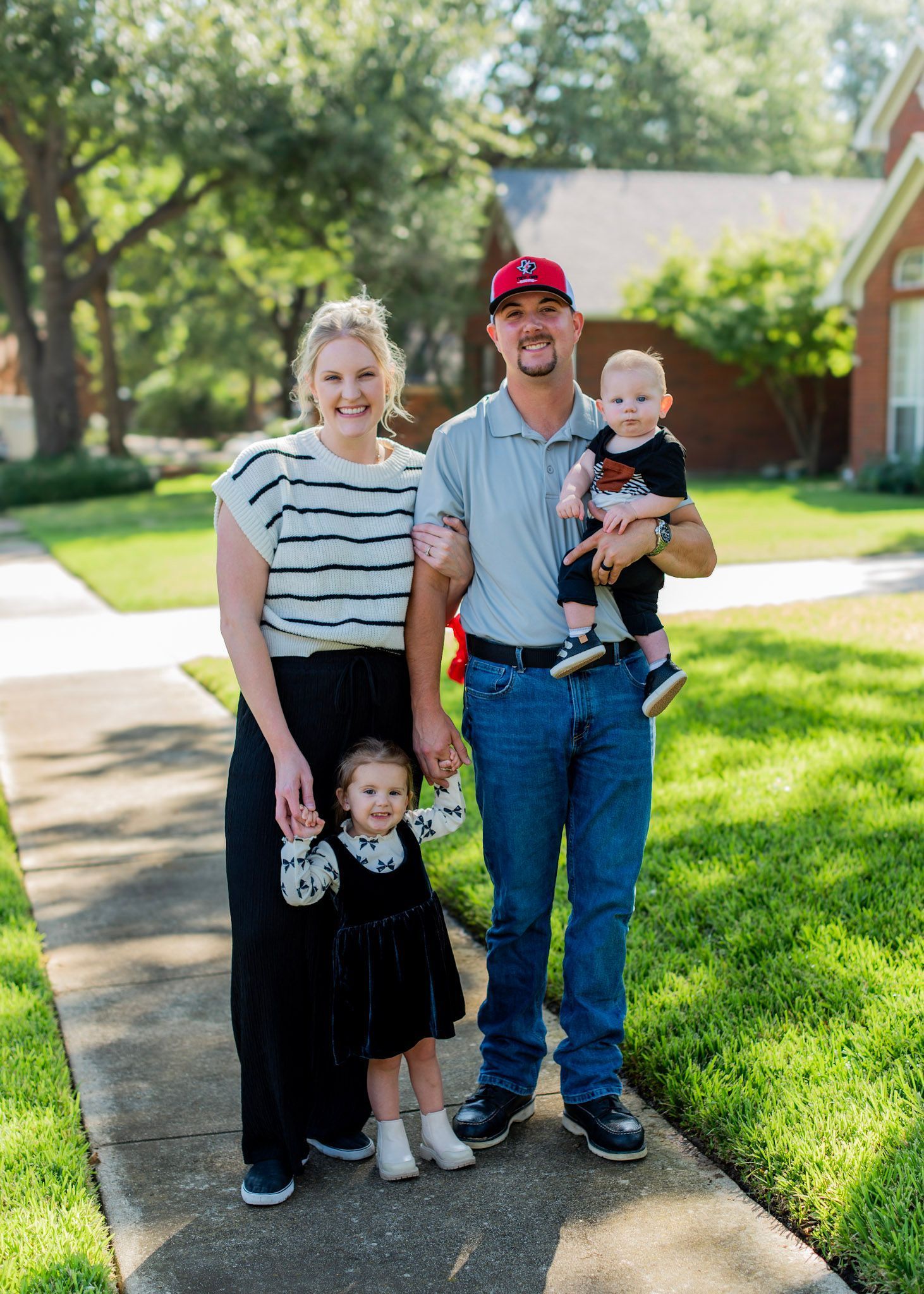 A family is posing for a picture on a sidewalk in front of a house.