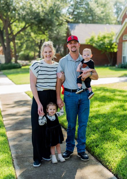 A family is posing for a picture on a sidewalk in front of a house.
