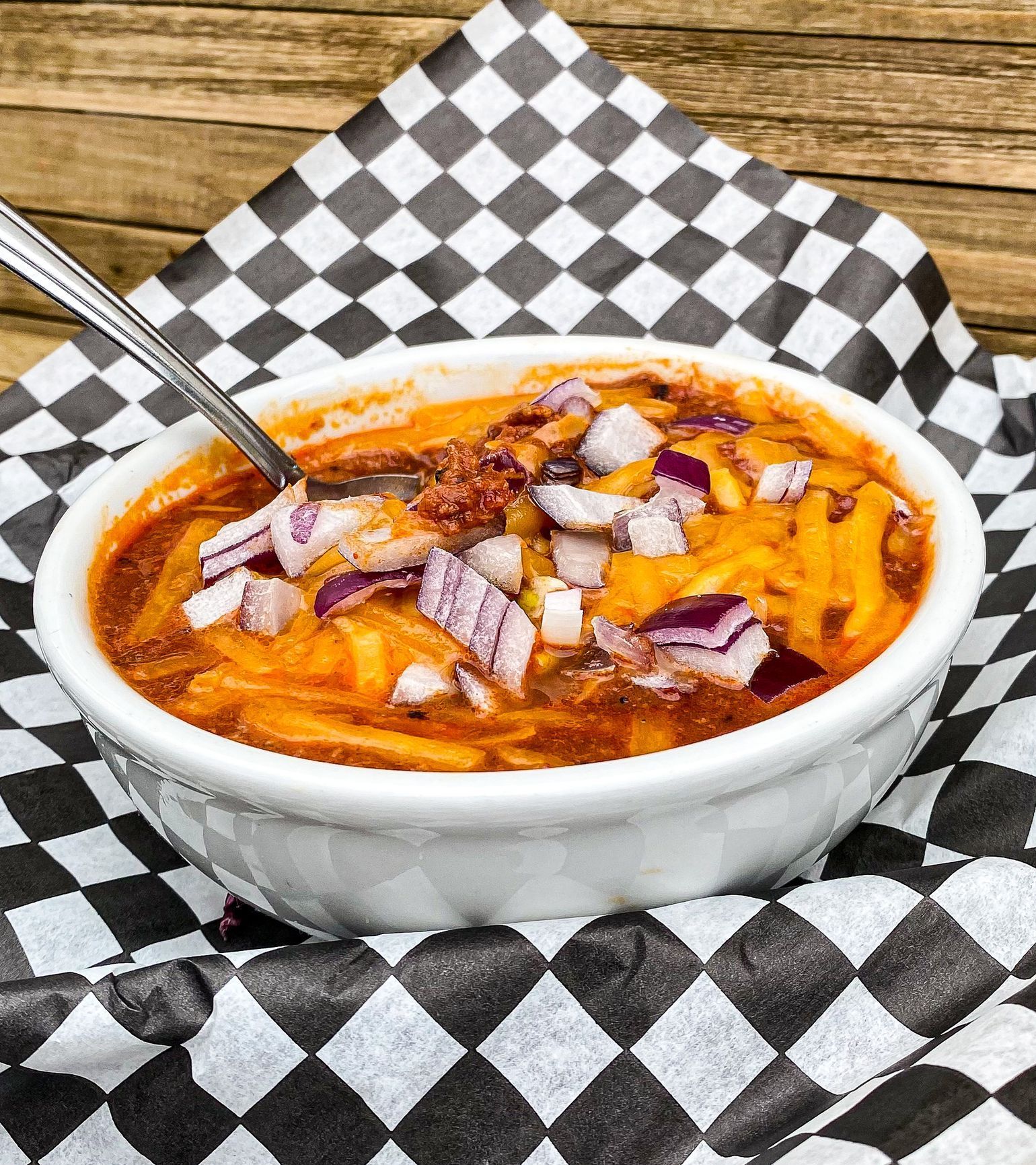 A bowl of chili with cheese and onions next to a piece of cornbread.