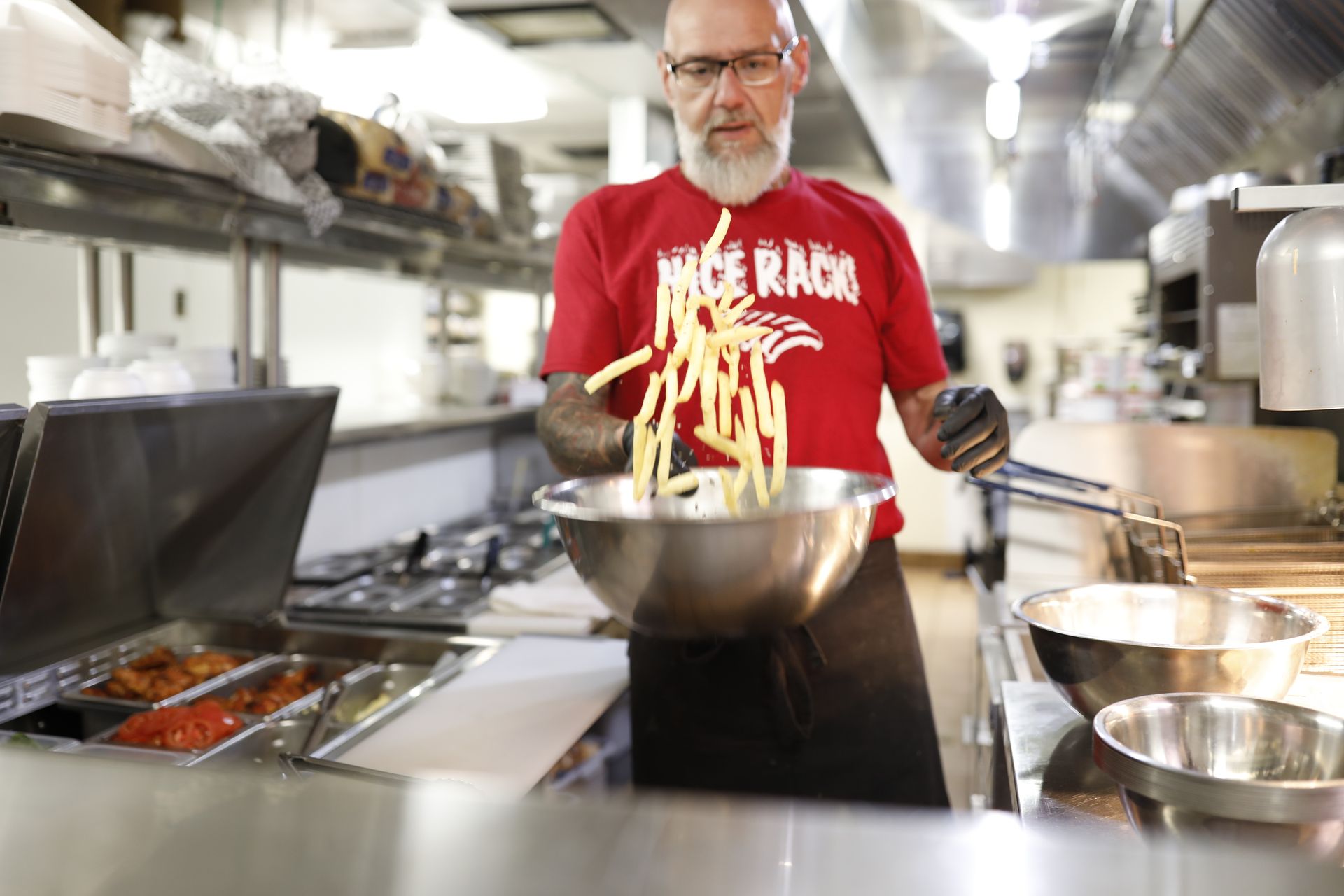A man in a red shirt is cooking french fries in a kitchen.