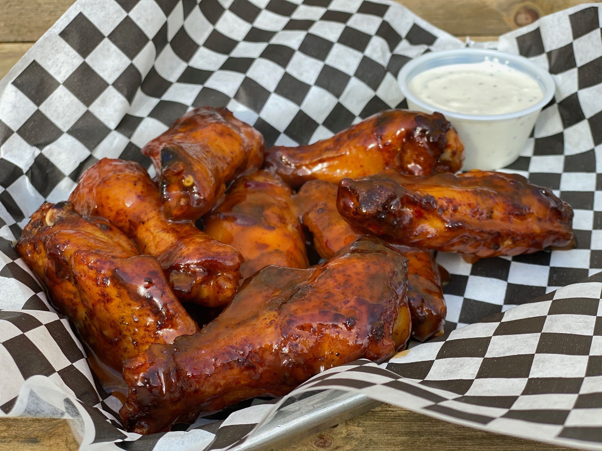 A basket of chicken wings with a dipping sauce on a checkered paper.